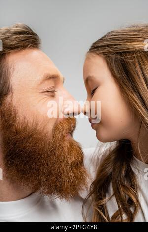 Seitenansicht eines bärtigen Vaters und einer jungen Tochter, die von Nase zu Nase stehen, isoliert auf grauem Stockbild Stockfoto