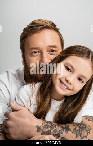 Porträt eines lächelnden Elternteils, das seine junge Tochter umarmt, isoliert auf grauem Stockbild Stockfoto