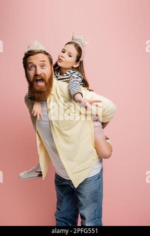 Das junge Mädchen zeigt eine Friedensgeste, während es seinen Vater auf einem pinkfarbenen Stock-Bild verprügelt Stockfoto