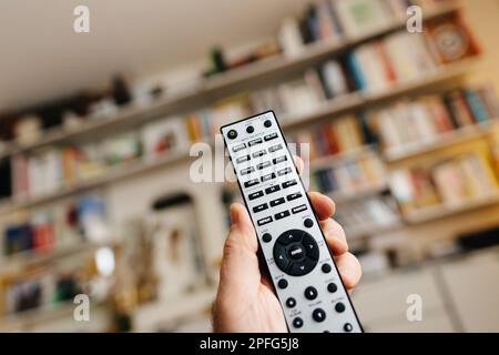 Frankfurt, Deutschland - 23. Februar 2023: Nahaufnahme POV männliche Hand mit neuer Fernsteuerung Onkyo RC-816C mit USB NET, CD, Phono und anderen Knöpfen im Wohnzimmer mit Vitsoe-Regalen im Hintergrund Stockfoto
