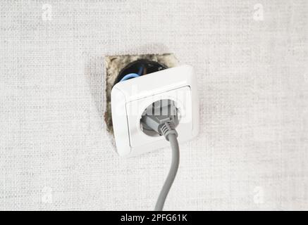 Gefährlich schlecht, kaputte Steckdose, Stecker im Badezimmer, fällt aus der Wand. Installation der Steckdose in der alten Wohnung. Schlechte elektrische Leitung, Reparatur. Schreckliches Do-it-you Stockfoto