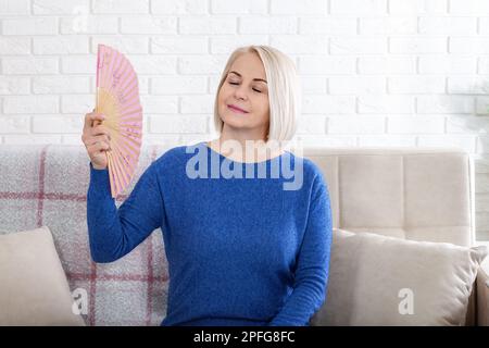 Reife Frau mit Hitzewallungen aus der Menopause. Dieses Foto zeigt die Beschwerden von Hitzewallungen in den Wechseljahren, während eine Frau kämpft, um sich abzukühlen Stockfoto