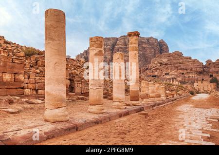 Rote Steinsäulen sind in der Colonnaded Street in Petra, Jordanien, in felsigen Bergen mit Höhlenlöchern im Hintergrund Stockfoto