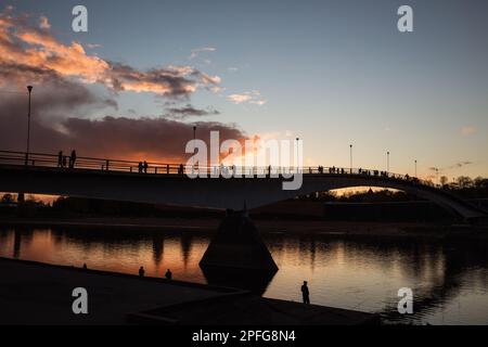 Silhouetten von Menschen auf der Fußgängerbrücke in Novgorod vor dem Sonnenuntergang mit rosa Wolken Stockfoto