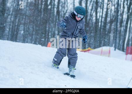 Kleiner Skifahrer, der bergab fährt und Schnee spritzt. Kinderski in den Bergen. Aktiver Teenager mit Schutzhelm, Schutzbrille und herunterfahrenden Skistöcken Stockfoto