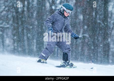 Kleiner Skifahrer, der bergab fährt und Schnee spritzt. Kinderski in den Bergen. Aktiver Teenager mit Schutzhelm, Schutzbrille und herunterfahrenden Skistöcken Stockfoto