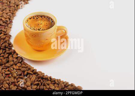 Schaumiger türkischer Kaffee in gelber Tasse neben Kaffeebohnen und weißem Hintergrund Stockfoto