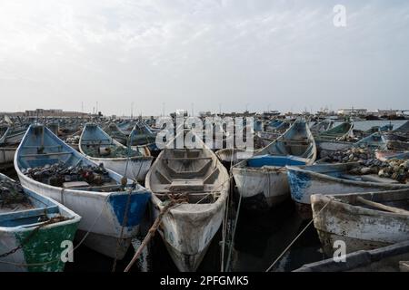 Eine Ansammlung von leuchtenden blau-weißen Fischerbooten in Nouadhibou, Mauretanien, die den maritimen Lebensstil und die Tradition dieses Fischerdorfes an der Küste einfangen Stockfoto