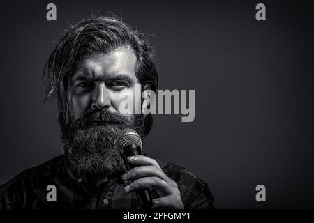 Ein bärtiger Mann, der mit dem Mikrofon singt. Männlicher Gesang mit einem Mikrofon. Ein Mann mit Bart, der ein Mikrofon hält und singt. Schwarz auf Weiß Stockfoto