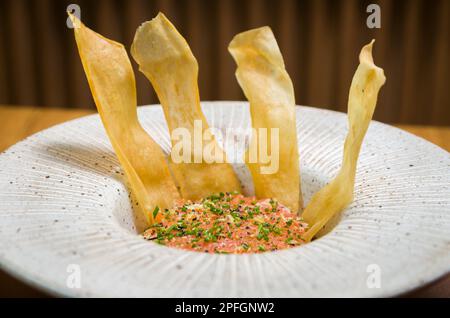 PERUANISCHES ESSEN. Gewürzter Lachs Ceviche mit Schnittlauch und Limette auf einem weißen Teller serviert mit gebratenen Süßkartoffeln Stockfoto