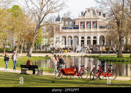 Touristen wandern und radeln im berühmten Vondelpark mit dem Vondelpark Pavillon im Hintergrund. Stockfoto