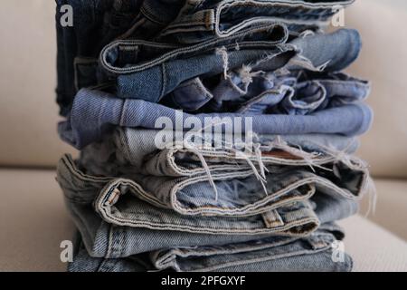 Organisierte Jeans-Hosen, ein Stapel Jeans in verschiedenen Farben auf einem weißen Sofa. Gefaltete Jeanshosen in einer Reihe auf einem weißen Sessel. Stockfoto
