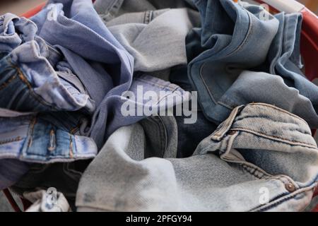 Ein Haufen Jeans Hosen, ein Haufen Jeans Hosen in einem roten, abgerundeten Korb. Ein Stapel Denimjeans Konzeptfoto. Nahaufnahme, Stockfoto