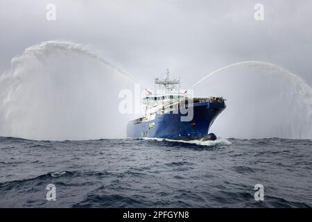 Schlepper zeigt Wasserabfluss. Ein Rettungsfeuerboot, das einen Wasserstrahl auf offenem Wasser auswirft. Feuerwehrschlauchboot sprüht Wasser auf das Meer für Unterstützung Stockfoto