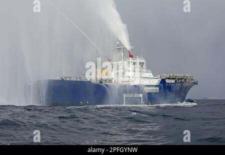 Schlepper zeigt Wasserabfluss. Ein Rettungsfeuerboot, das einen Wasserstrahl auf offenem Wasser auswirft. Feuerwehrschlauchboot sprüht Wasser auf das Meer für Unterstützung Stockfoto