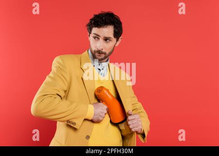 Modisches Modell, das den Lautsprecher in der Jacke versteckt, isoliert auf korallenrotem Stockbild Stockfoto