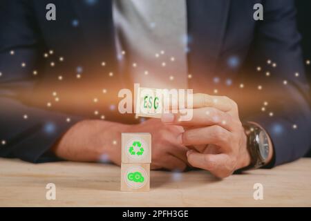 Geschäftsmann, der ESG-Holzwürfel auf den Tisch hebt. ESG-Umweltkonzept und soziale Governance. Nachhaltige Unternehmensentwicklung. Stockfoto