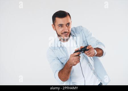 Hält den Joystick in den Händen. Junger, gutaussehender Mann, der drinnen vor weißem Hintergrund steht Stockfoto