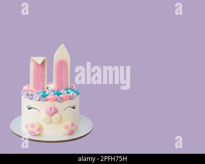 Weißer und rosafarbener Kuchen mit niedlichem Häschen zum Geburtstag oder zu Ostern. Violetter Hintergrund. Horizontale Ausrichtung Stockfoto