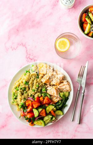 Gesundes Mittagessen, Quinoa mit grünen Erbsen, gebackener roter Fischlachs und frischer Salat mit Tomaten, Gurken und Grüns, Draufsicht Stockfoto