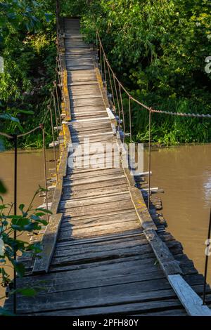 Hängende Holzbrücke auf die andere Seite des Flusses. Hängebrücke in einem kleinen Dorf. Stockfoto