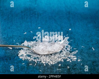 Ein Metalllöffel gefüllt mit natürlichen Menthol-Kristallen auf blauem Hintergrund. Stockfoto