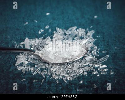 Ein Metalllöffel gefüllt mit natürlichen Menthol-Kristallen auf blauem Hintergrund. Stockfoto