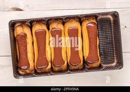 Mehrere Schokoladeneclairs mit Plastikschale auf Holztisch, Nahaufnahme, Draufsicht. Stockfoto