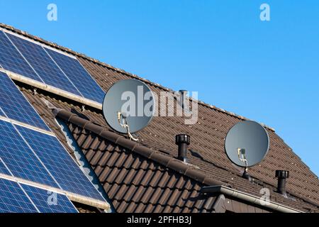 Zwei Satellitenschüsseln auf dem Dach eines gefliesten Hauses. Sonnenkollektoren auf dem Dach. Klarer blauer Himmel. Stockfoto