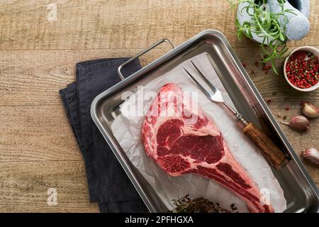 Frisches rohes Tomahawk-Steak. Trocken gereiftes rohes Tomahawk-Rindersteak mit Kräutern und Salz auf altem Holzhintergrund. Grillvorgang wird vorbereitet. Draufsicht und Kopierbereich. Stockfoto