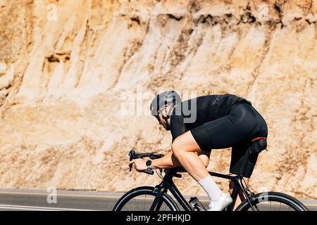 Triathleten fahren mit dem Road Bike im Freien. Muskelradfahrer in schwarzer Sportbekleidung. Stockfoto