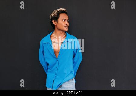 Junger, stylischer Typ in blauem Hemd, der an der schwarzen Wand posiert Stockfoto