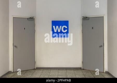 Blaues WC-Schild an der weißen Wand mit zwei Toilettentüren auf jeder Seite Stockfoto