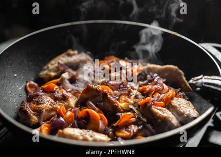 Rohes Kaninchen mit Gewürzen, Zwiebeln und Karotten in einer Pfanne. Ich koche gedünstetes Kaninchen. Stockfoto