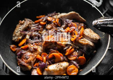 Rohes Kaninchen mit Gewürzen, Zwiebeln und Karotten in einer Pfanne. Ich koche gedünstetes Kaninchen. Stockfoto