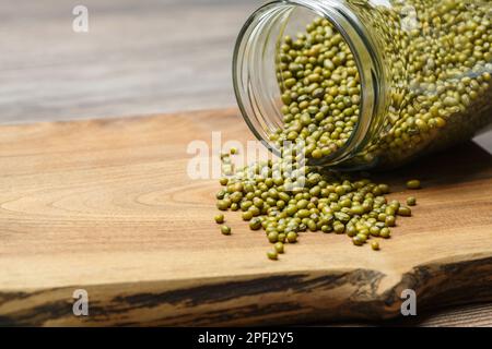 Grüne Mungo-Bohnen, die aus einem Glasgefäß auf einem Holzhintergrund herauskommen. Mikrogrün und vegan gesundes Food-Konzept. Stockfoto