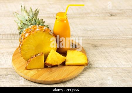 Scheiben saftiger Ananas und ein frischer, gesunder Smoothie in einer Glasflasche und einem Strohhalm auf einem Holzbrett auf Holzhintergrund. Gesund, Entgiftung Stockfoto