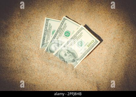 Gelddolare, die halb mit Sand bedeckt sind, liegen in der Nähe des Strandes. Dreihundert Dollar im Sand auf Meer oder Meer Strand begraben Konzept finanzieren Geld Urlaub entspannen Urlaub. Sonniger Sommer warmer Windtag. Stockfoto