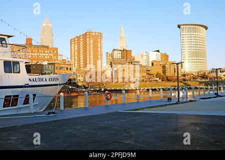 Die Nautica Queen verlegte vor der westbank des Cuyahoga River, während die Sonne im Winter über der Ostbank und der Skyline von Cleveland unterging. Stockfoto