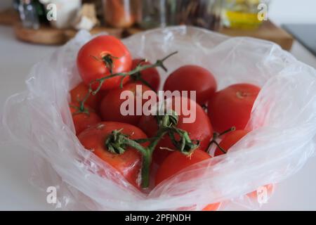 Einige faule Tomaten und einige unberührte Tomaten befinden sich in einem durchsichtigen Plastikbeutel auf einer weißen Küchenarbeitsfläche. Stockfoto