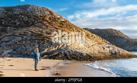 Glückliche Frau am Ufer des Nordatlantiks, an einem knappen Wintertag, ohne Schnee an der Küste. Stürmisches Wetter mit Inseln in Hillesøya, Norwegen Stockfoto