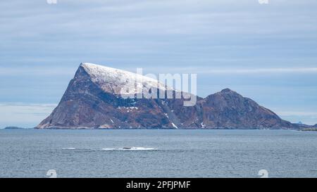 Stürmischer Ozean am Ufer von Hillesøya, in Troms, Norwegen, mit Wellen an der Küste kleiner Inseln, mit schneebedeckten Bergen im Hintergrund. Stockfoto