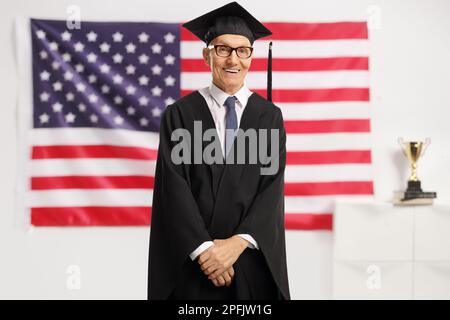 Ein älterer Absolvent trägt ein Kleid und lächelt mit einer US-Flagge dahinter Stockfoto