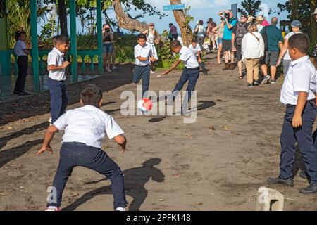 Tortuguero, Costa Rica - während Touristen vorbeilaufen, spielen Schuljungen in diesem kleinen Dorf an der Karibikküste vor ihrer Schule Fußball. Co Stockfoto