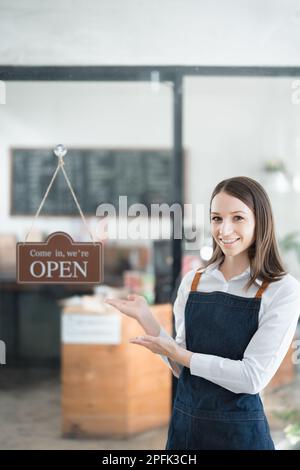 Eine junge asiatische Frau, die ein kleines Unternehmen eröffnete und ein lächelndes Gesicht auf einer Schürze vor einer Theke der Café-Bar zeigte. Unternehmen Stockfoto