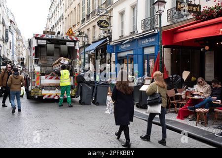 PARIS, FRANKREICH - MÄRZ 17: Arbeiter sammeln Müll von der Straße neben einem Restaurant, während die Leute während eines Streiks von Müllarbeitern über die Anhebung des Rentenalters durch die Regierung am 17. März 2023 in Paris Frankreich sitzen (Kredit: Jeremy O'Donnell) Kredit: Jeremy ODonnell/Alamy Live News Stockfoto