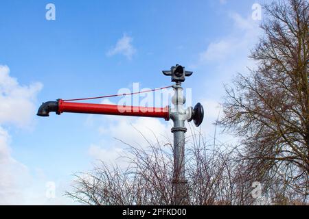 Roter Wasserhahn am Hintergrund des Himmels. Hydrant mit Wasserhahn und Absperrarmatur Stockfoto