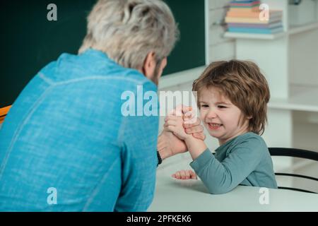 Vater und Sohn ringen und lächeln, während sie zu Hause Zeit miteinander verbringen. Vater und Sohn bei freundlichem Armdrücken-Wettkampf zu Hause. Die Stockfoto