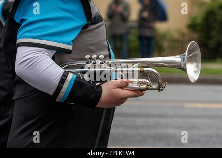 Ein Tromphet-Spieler der Marschkapelle hält während der Straßenparade ein Messinginstrument an der Seite. Stockfoto