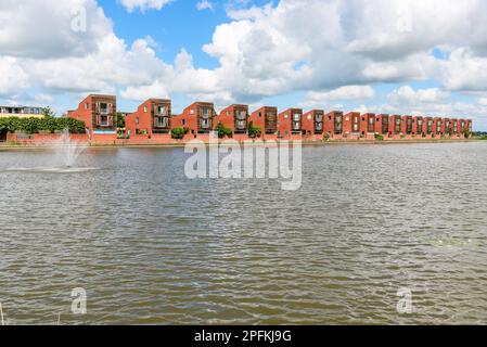 Eine Reihe moderner Häuser in einer Wohnanlage neben einem Teich an einem teilweise bewölkten Sommertag Stockfoto